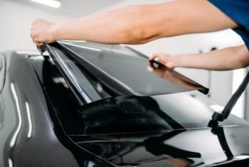 Male specialist with car tinting film in hands. Installation process, tinted auto glass installing procedure. Male specialist with car tinting film in hands