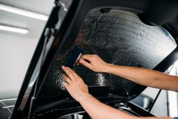 Male specialist with drier, car tinting film installation process, tinted auto glass installing procedure. Specialist with drier, tinting film installation