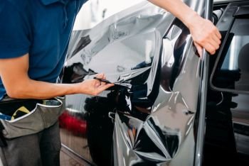 Male specialist with scissors, car tinting film installation process, tinted auto glass installing procedure. Male specialist with scissors, car tinting film