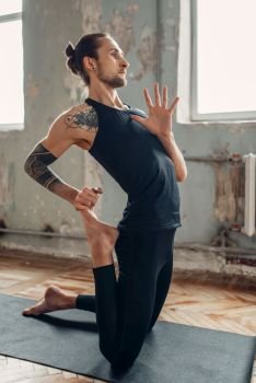 Male yoga in class, flexibility training. Exercise on mat in gym with grunge interior. Fit workout indoors