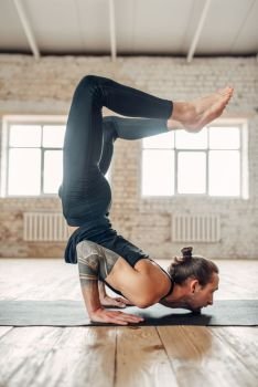 Male yoga standing on hands upside down. Exercise on mat in gym with grunge interior. Fit workout indoors. Male yoga standing on hands upside down