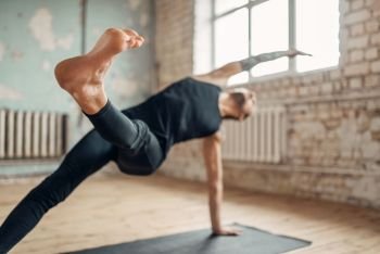 Yoga training on mat in studio with grunge interior. Fit workout indoors, yogi studio, male athlete doing stretching exercise