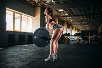 Muscular female athlete training with barbell in sport gym. Woman exercise with weight in fitness club. Female athlete training with barbell in sport gym