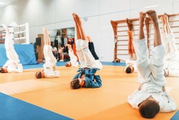Children karate, kids in kimono practice martial art in gym. Little boys and girls in uniform makes upside down exercise on sport training
