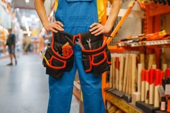 Male builder trying on tool belt at the shelf in hardware store. Constructor in uniform look at the goods in diy shop. Male builder trying on tool belt in hardware store