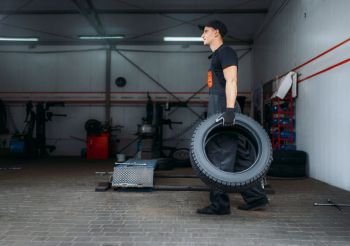 Auto mechanic holds two new tires, repairing service. Worker repairs car tyre in garage, professional automobile inspection in workshop. Auto mechanic holds two tires, repairing service