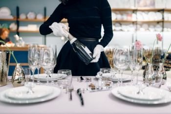 Waitress with a bottle of champagne, table setting. Serving service, festive dinner decoration, holiday dinnerware