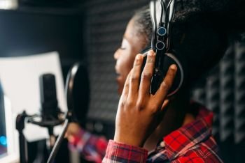 Young woman in headphones songs in audio recording studio. Musician listens composition, professional music mixing. Young woman songs in audio recording studio
