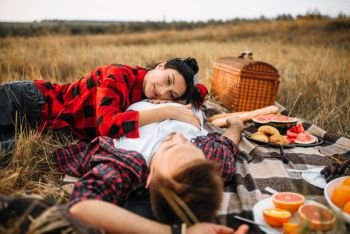 Love couple lies on plaid, picnic in summer field. Romantic junket of man and woman. Love couple lies on plaid, picnic in summer field