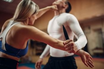 Woman makes punch to the throat, self-defense workout with male personal trainer, gym interior on background. Female person on training, self defense practice. Woman makes punch to the throat, self-defense