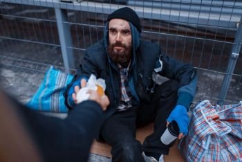 Male person gives food to bearded dirty beggar on city street. Poverty is a social problem, homelessness and loneliness, alcoholism and drunk addiction, urban lonely. Male person gives food to bearded dirty beggar