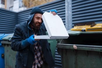 Bearded dirty beggar found pizza in trashcan on city street. Poverty is a social problem, homelessness and loneliness, alcoholism and drunk addiction, urban lonely. Bearded dirty beggar found pizza in trashcan