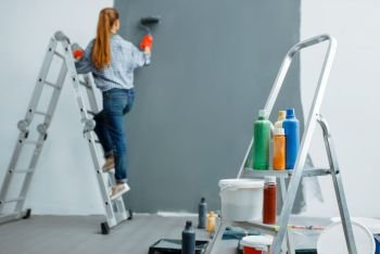 Female house painter paints walls indoor. Home repair, laughing woman doing appartment renovation, room decoration renovating. Female house painter paints walls indoor