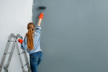 Female house painter paints walls indoor. Home repair, laughing woman doing appartment renovation, room decoration renovating. Female house painter paints walls indoor