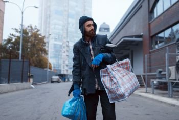 Bearded tramp man with bag on city street. Poverty is a social problem, homelessness and loneliness, alcoholism and drunk addiction, urban lonely. Bearded tramp man with bag on city street