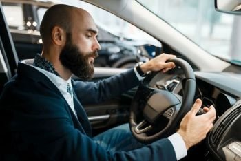 Man behind the wheel of new automobile in car dealership. Customer in vehicle showroom, male person buying transport, auto dealer business. Man behind the wheel of automobile, car dealership