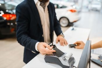 Man pays for the purchase of a new auto in car dealership. Customer and saleswoman in vehicle showroom, male person buying transport, automobile dealer business. Man pays for new auto in car dealership