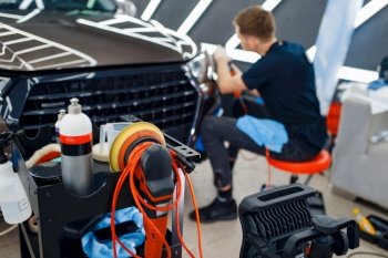 Male worker polishes headlights using polishing machine, car detailing. Preparationa before installation of coating that protects the paint of automobile from scratches. Auto tuning in workshop. Male worker polishes headlights, car detailing