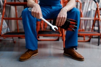 Male employee in uniform holds wrench in tool store. Choice of professional equipment in hardware shop, instrument supermarket. Male employee in uniform holds wrench, tool store