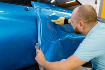 Car wrapper installs protective vinyl foil or film on vehicle door. Worker makes auto detailing. Automobile paint protection, professional tuning. Car wrapper installs protective vinyl foil or film