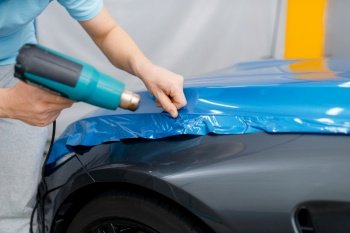 Car wrapping, mechanic with drier installs protective vinyl foil or film on vehicle hood. Worker makes auto detailing. Automobile paint protection coating, professional tuning. Car wrapping, mechanic with drier installs film