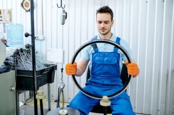 Worker in uniform holds new aluminum bicycle rim on factory. Bike wheels assembly in workshop, cycle parts installation. Worker holds new aluminum bicycle rim on factory