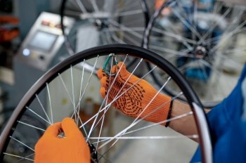 Worker in gloves installs new bicycle spokes on factory. Bike wheels assembly in workshop, cycle parts installation, modern technology. Worker in gloves installs bicycle spokes, factory
