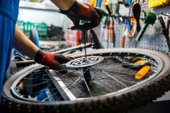Bicycle assembly in workshop, man installs brake disk. Mechanic in uniform fix problems with cycle, professional bike repairing service. Bicycle assembly in workshop, man installs brake