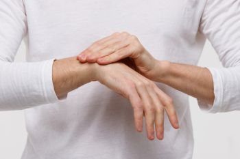 Close up of man arms holding her painful wrist caused by prolonged work on the computer, laptop. Carpal tunnel syndrome, arthritis, neurological disease concept. Numbness of the hand