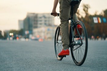 Closeup of casual man legs riding classic bike on city gray road wearing red sneakers and comfy pants. Copy space. Closeup of casual man legs riding classic bike on city road