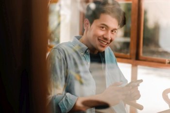 Happy Young Man Smiling and  Looking at Camera through Glass Window while Sitting in Cafe