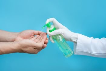 Hand in medical gloves applying sanitizer gel onto men hands for protection against infectious virus, bacteria and germs in blue background