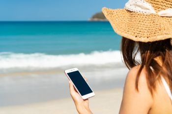 Happy traveller Asian woman  enjoys at tropical beach while using smart phone on vacation. Summer on beach concept.