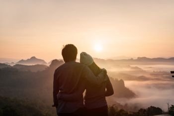 Young couple traveler looking at sea of mist and sunset over the mountain at Mae Hong Son, Thailand. Young couple traveler looking at sea of mist and sunset over the mountain