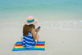 Young woman relaxing and using mobile phone at the tropical beach, Summer vacation and travel concept