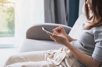 Young woman siiting on sofa and using smart phone at home
