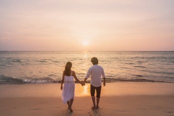 Young woman traveler holding man’s hand and looking beautiful sunset on the beach, Couple on vacation in summer concept