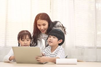 Happy young Asian family with children and their mother using computer do school homework at home.