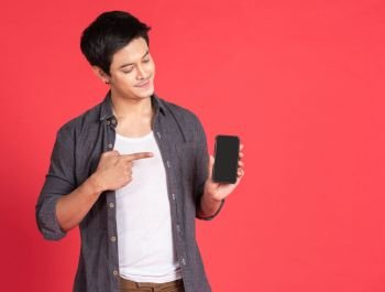 Portrait of young attractive asian businessman or student using mobile phone, laptop, tablet, standing isolated on red background wearing casual shirt look at camera in studio with copy space.