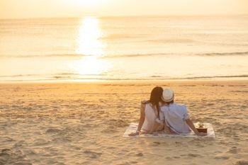 Couple in love watching sunset together on beach travel summer holidays. People silhouette from behind sitting enjoying view sunset sea on tropical destination vacation. Romantic couple on the beach.