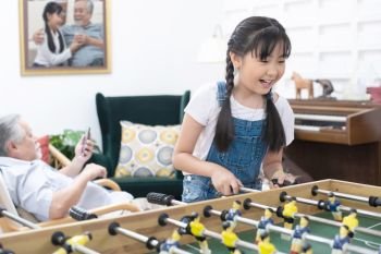 Young happy asian girl playing soccer table game together happiness. Grandmother and grandfather sit relax in living room in home after retirement daily lifestyle. Happy leisure time family concept.