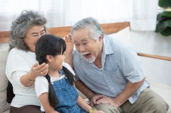 Happy asian elder happy  grandfather head touch granddaughter head while sit on sofa and have leisure time together at home.