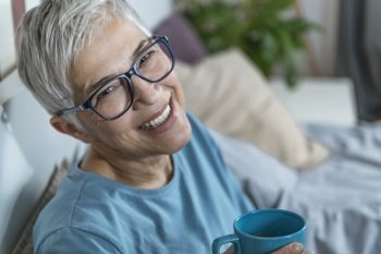 Smiling Mature Woman Lying in Bed, Drinking Coffee and Talking Over the Phone Before Sleep