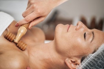 Maderotherapy anti-aging treatment of upper part of a woman’s neck and torso with wooden roller . Maderotherapy Anti-Aging Treatment of Woman’s Neck and Torso with Wooden Roller