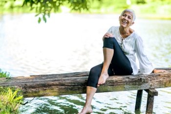 Beautiful, mindful, mature woman sitting by the water, enjoying peace and tranquility of the nature. Beautiful mature woman enjoying peace and tranquility of the nature