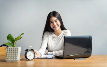 Work from home during the outbreak of the virus. Asian women sitting and working at home or online meeting, video conference and Writing data in a book in business concept at home office