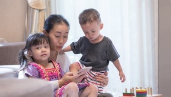 Asian mother with 2 children are relaxing on the sofa and looking smart phone with a surprised expression on her face in living room at home