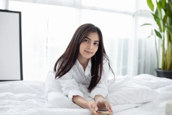 Asian woman Smile feel carefree and she lying on the bed in the morning and young beautiful girl will listening to music on headphones