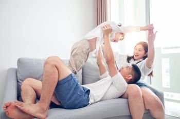 Happy Asian family with son at home on the sofa playing and laughing 