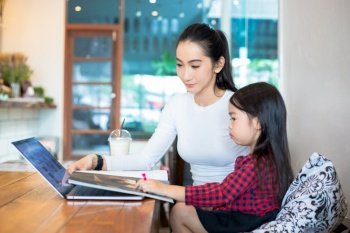 Asian mothers are teaching their daughters to read a book and use notebooks and technology for online learning during school holidays at home. Educational concepts and activities of the family